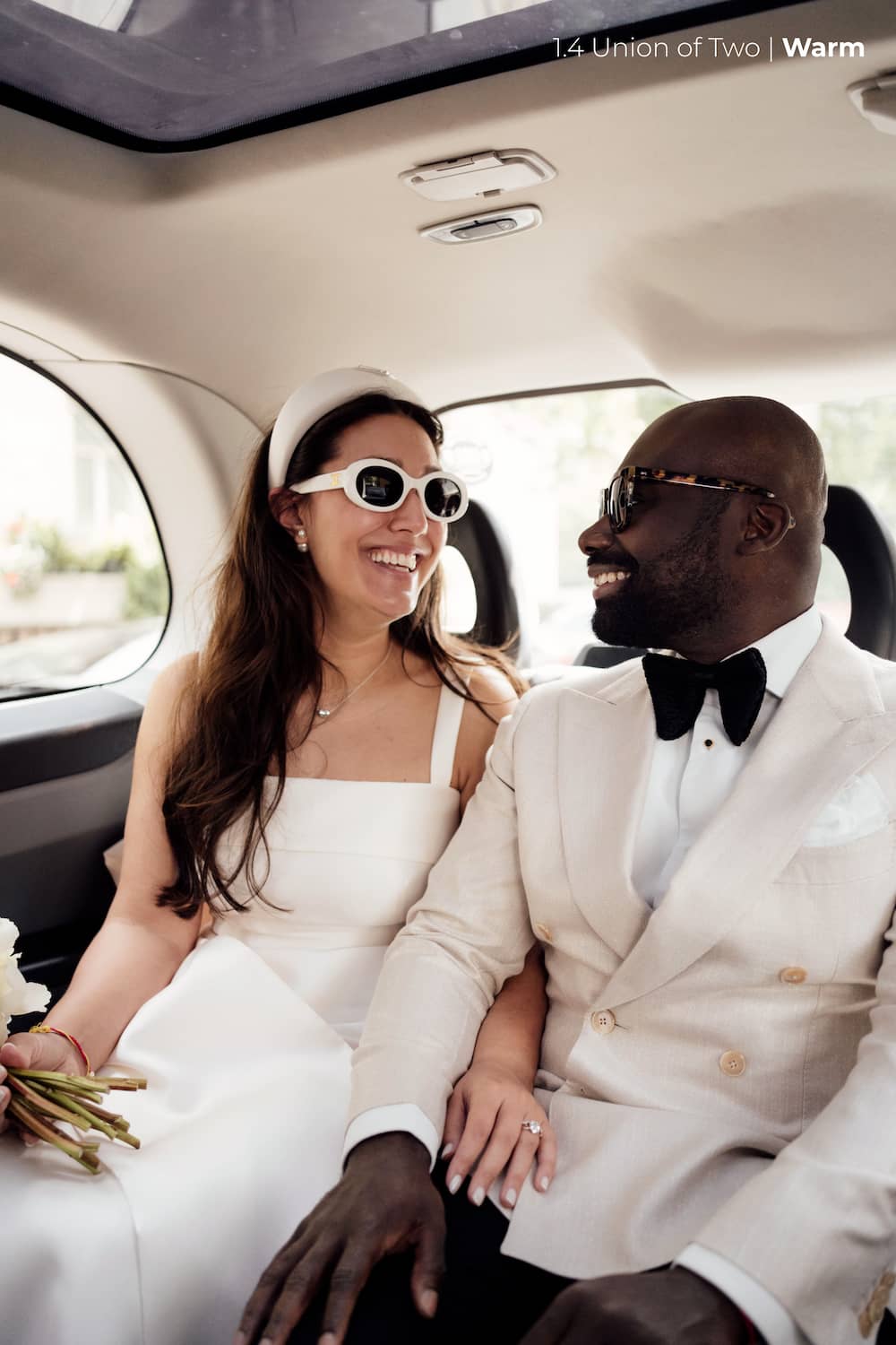 A bride in a white dress, headband and sunglasses smiles at her groom in a white tuxedo as they sit in the back of a london taxi, edited with the Union of Two 2.0 Preset Pack.